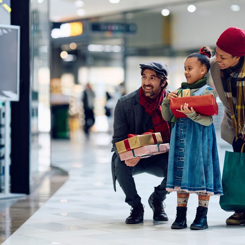 Happy family looking at store windows while buying Christmas present at shopping mall.