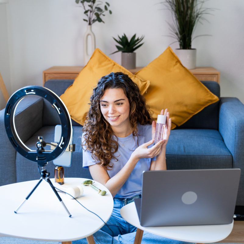 Image: Curly-haired woman showcasing skincare products on camera.