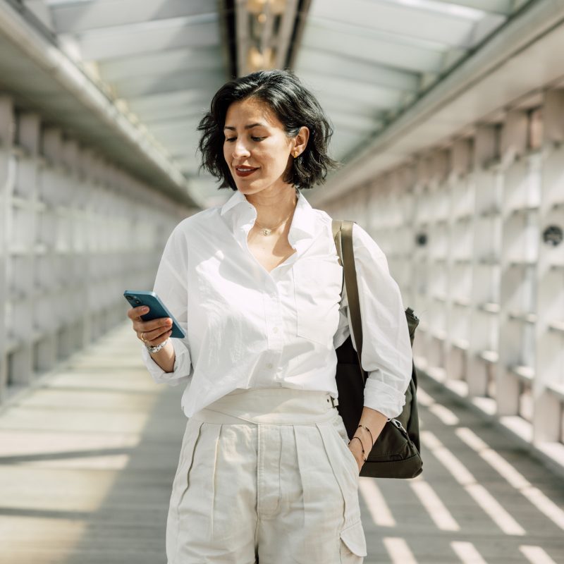 Image: Woman in business dress walking and using phone.