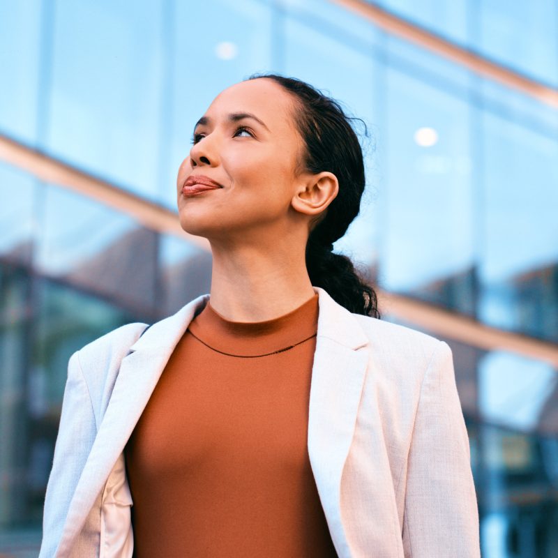 Confident businesswoman standing outdoors in front of a modern glass building, exuding professionalism and success.