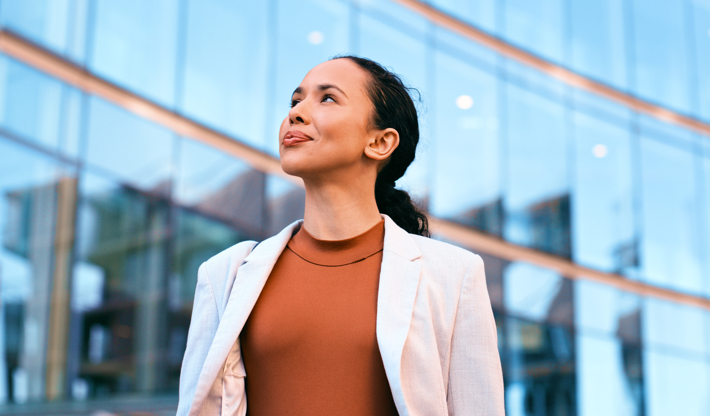 Confident businesswoman standing outdoors in front of a modern glass building, exuding professionalism and success.